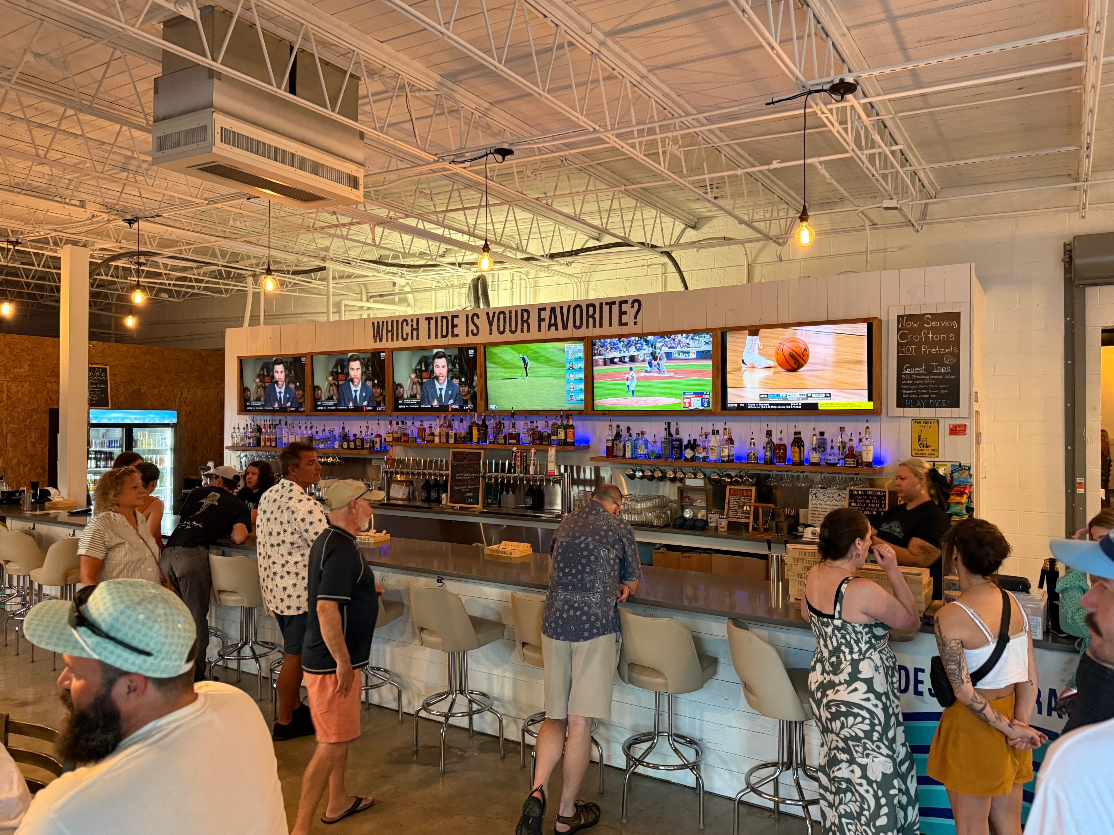 People in a casual setting at Tides Taproom with multiple televisions displaying sports content.