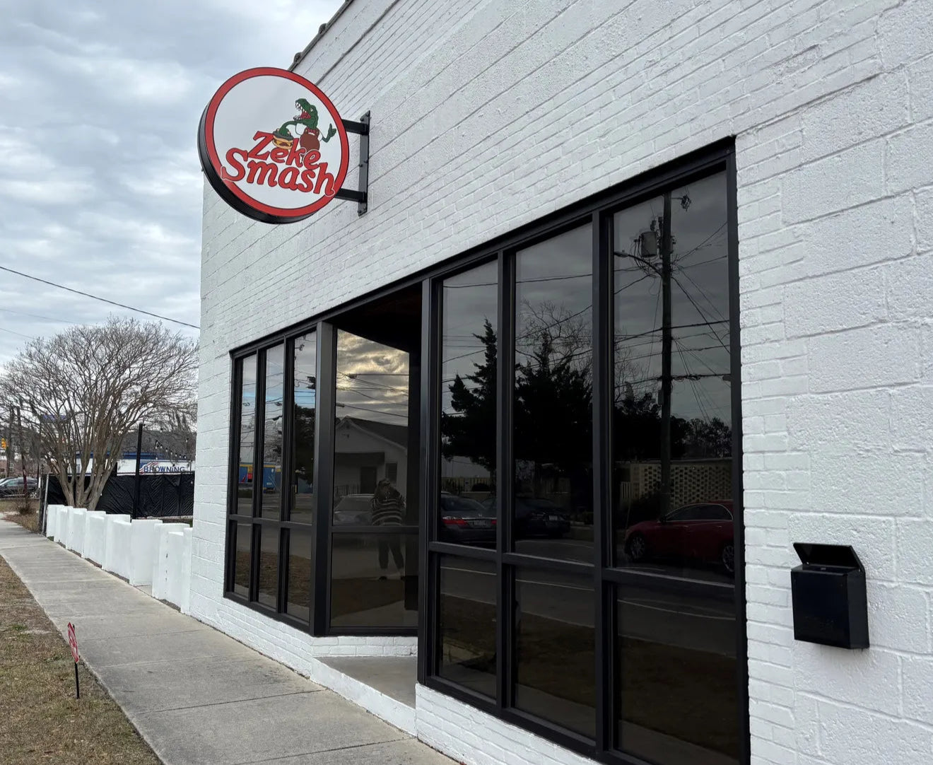 White brick building with a large window and 'Zeke Smash' sign on a cloudy day.